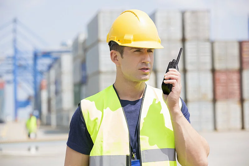 Mann in Containerhafen benutzt ein mobiles Endgerät